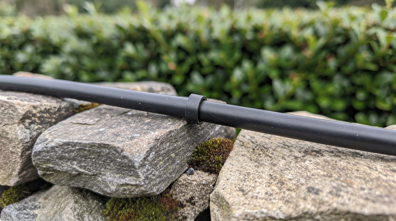 Black solar cable running along a stone wall with green hedge behind in an Irish countryside garden.